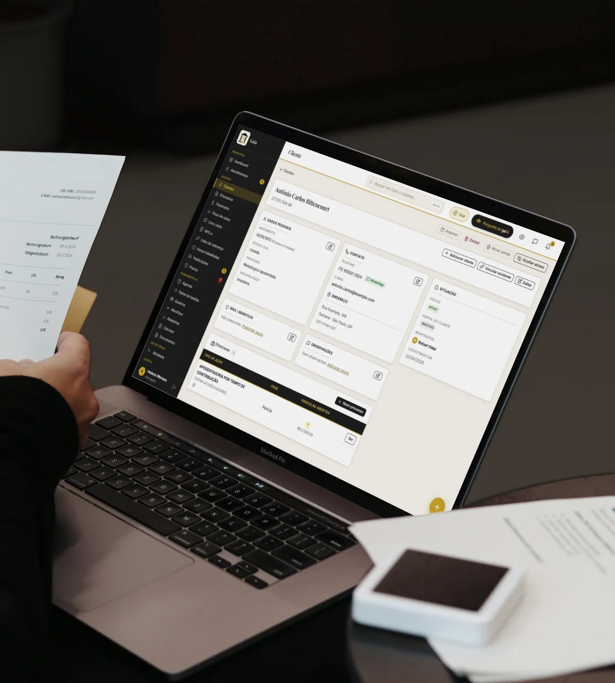 Advogado conferindo documentos ao lado do notebook com a ficha de um cliente aberta no Gaia